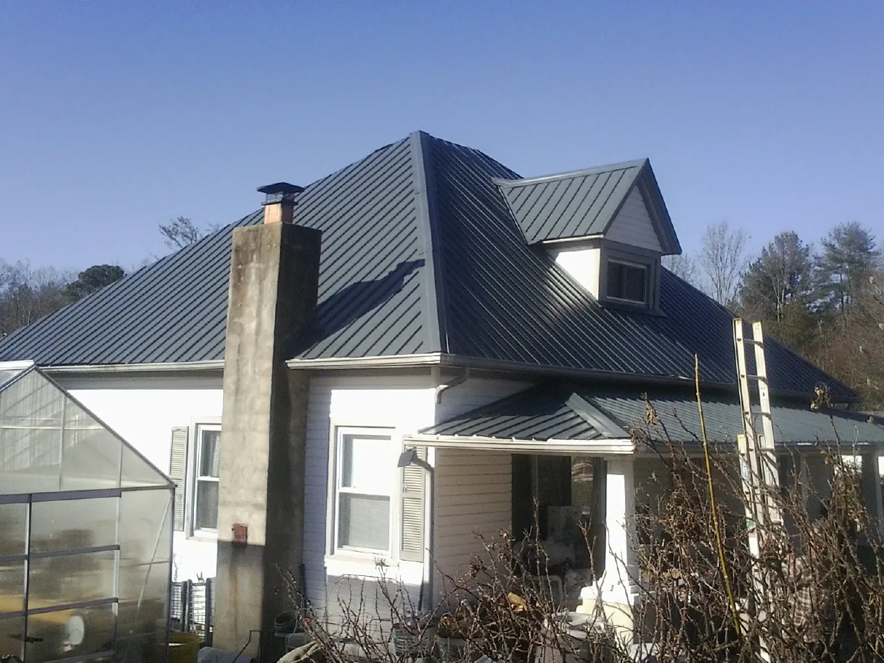 Dark blue standing seam metal roof on a white farmhouse with dormer — Slate & Tile Roof Repair by Roofing Brothers in Falls City