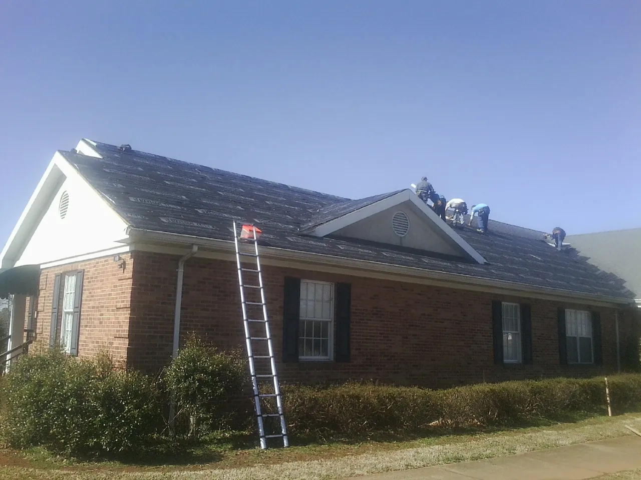 Crew tearing shingles off a brick ranch roof with a ladder set — Metal Roof Repair work by our crew in Falls City