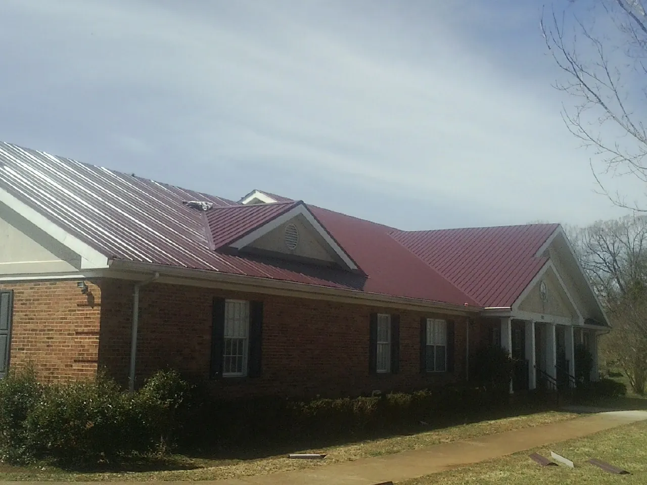 Red metal roof with gabled entries on a long brick building, from a Hail Damage Roof Repair job in Falls City