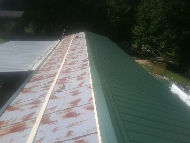 Old rusted panels beside newly installed green metal roofing — Wind Damage Roof Repair by Roofing Brothers in Falls City