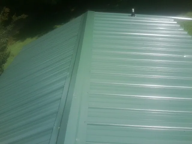 New green metal panels meeting at the ridge of a roof — Flat Roof Repair work by our crew in Falls City
