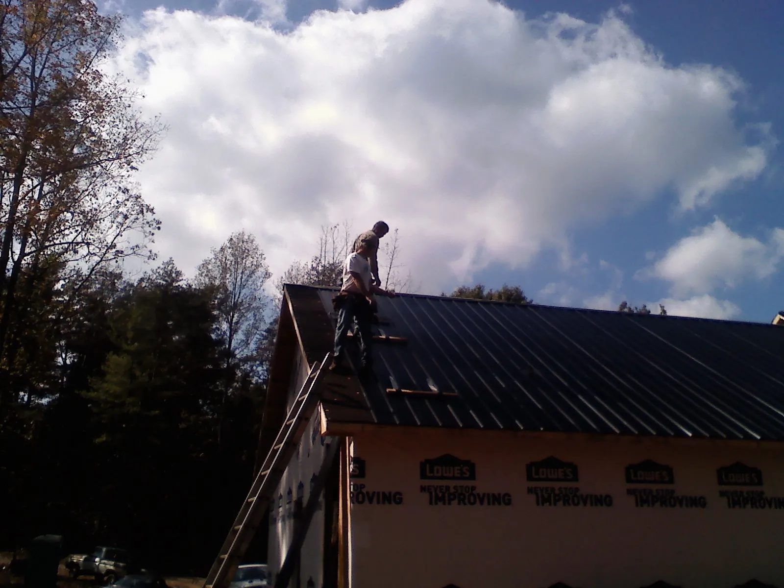 Roofer fastening dark metal panels high against a cloudy sky, from a Roof Inspection job in Falls City