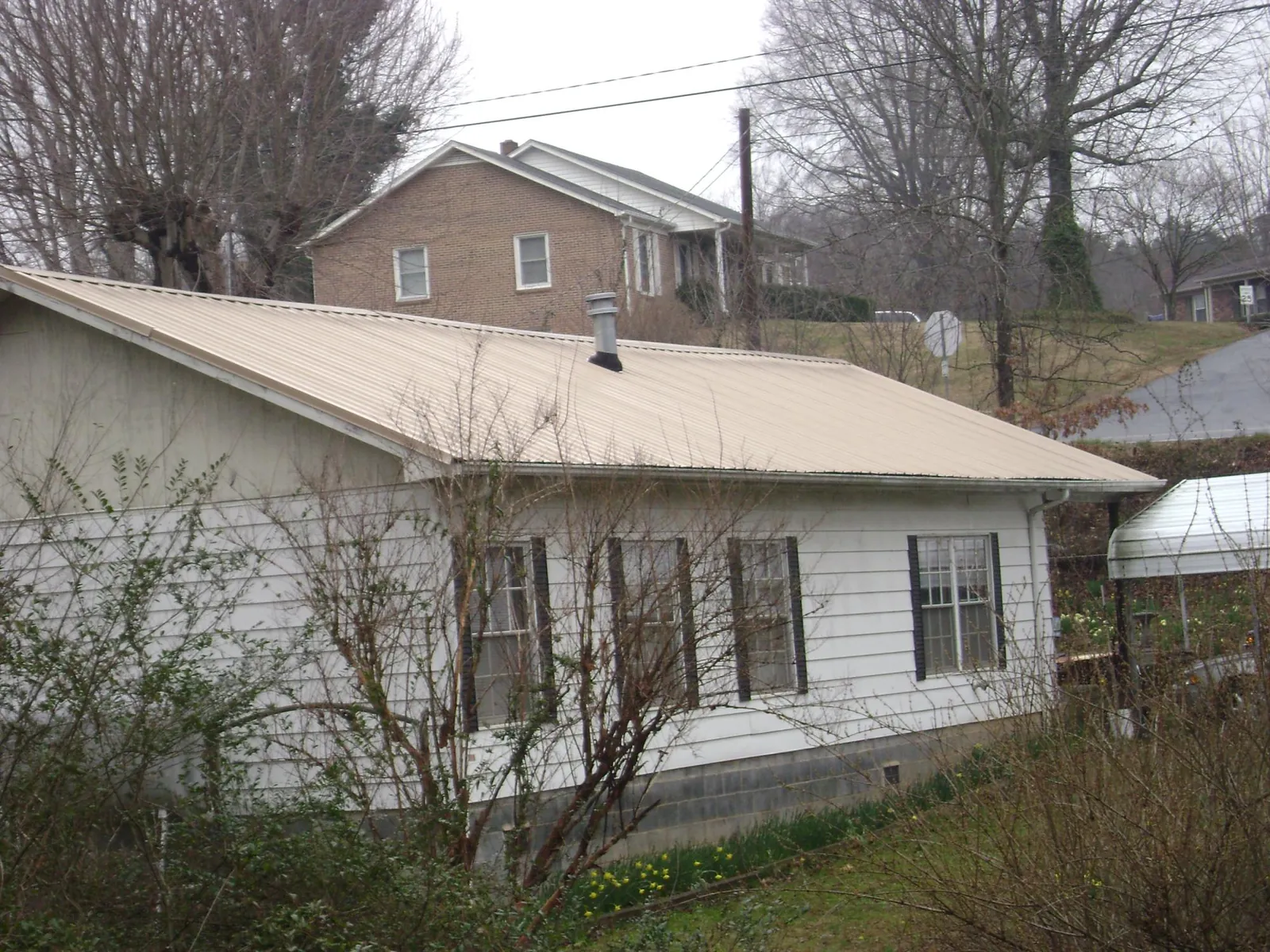 Tan metal roof on a white sided house set into a hillside — Commercial Roofing by Roofing Brothers in Falls City