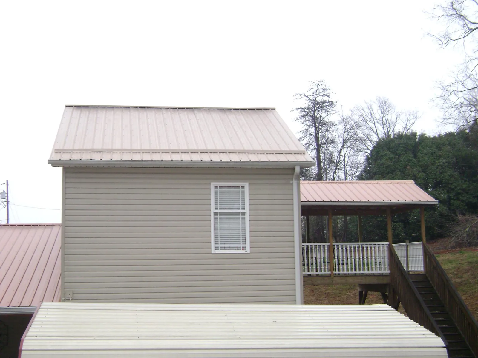 Tan metal roofs on a two story addition and attached porch, from a Roof Replacement job in Falls City